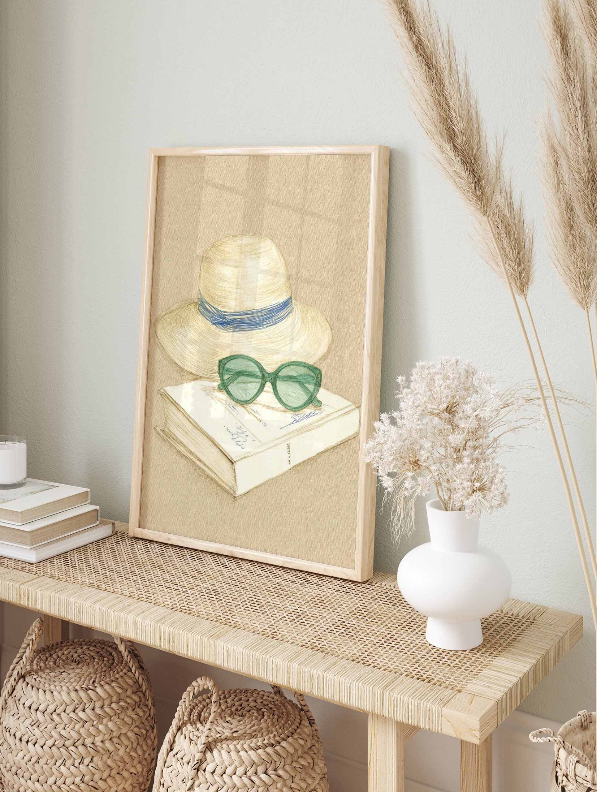 Sketch illustration of a straw hat with blue ribbon, green sunglasses, and a book on a beige, in an alternate framed mockup