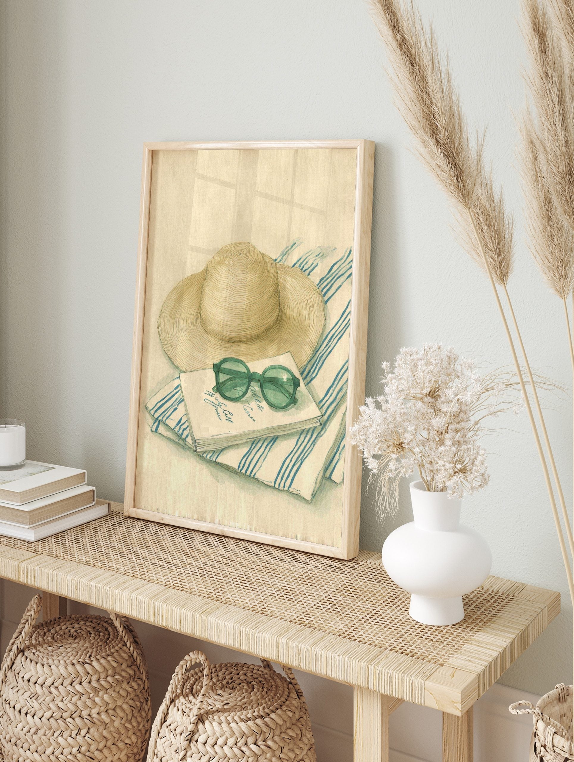 Illustrative print of a straw hat, round green sunglasses, and a notebook on a blue and white, in an alternate framed mockup