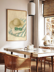 Illustrative print of a straw hat, round green sunglasses, and a notebook on a blue and white, in a styled room mockup