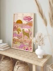 Illustrative striped cat in a pink and gold desert landscape with patterned hills and a, in an alternate framed mockup