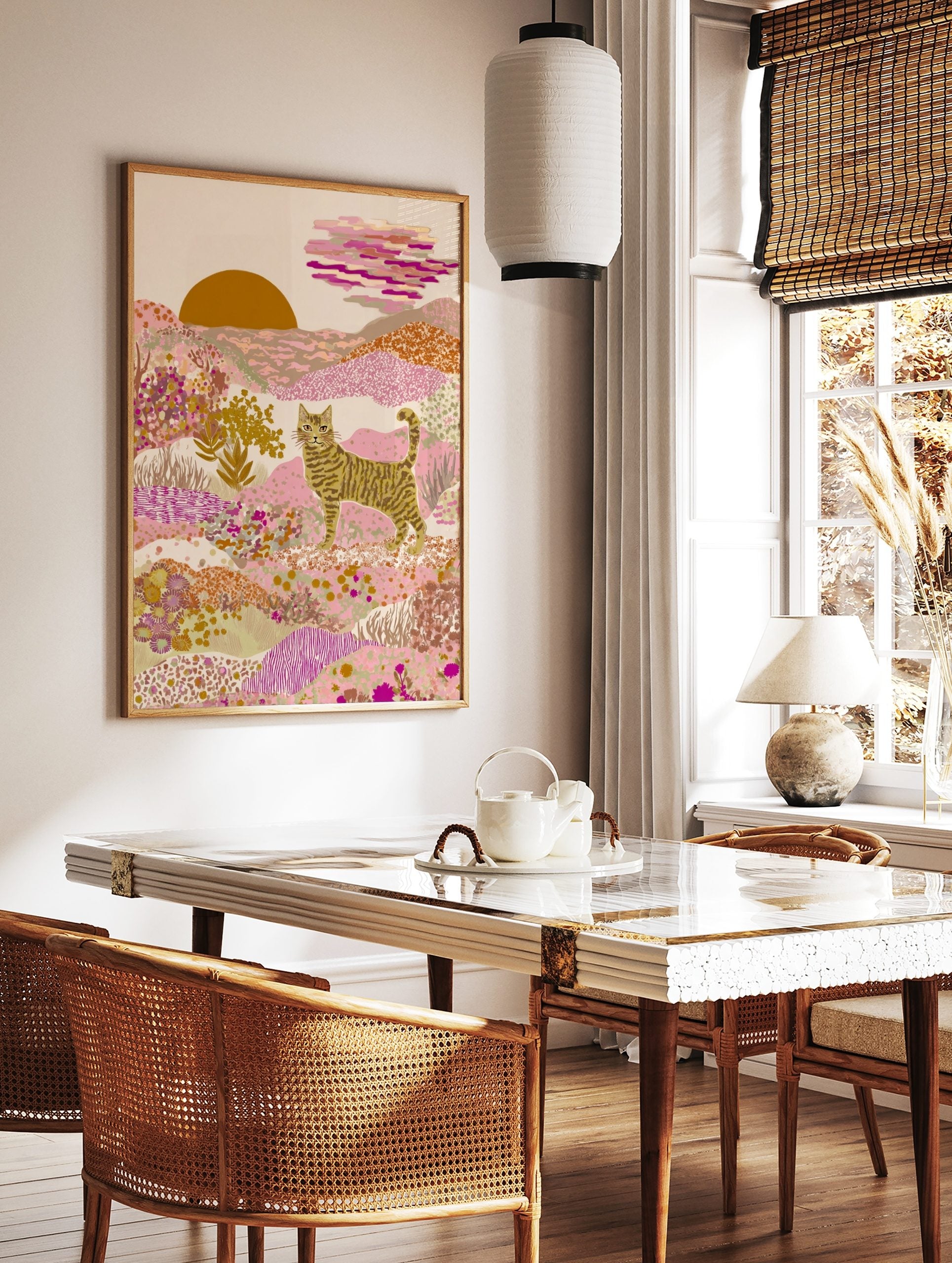Illustrative striped cat in a pink and gold desert landscape with patterned hills and a setting sun, in a styled room mockup