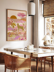 Illustrative striped cat in a pink and gold desert landscape with patterned hills and a setting sun, in a styled room mockup
