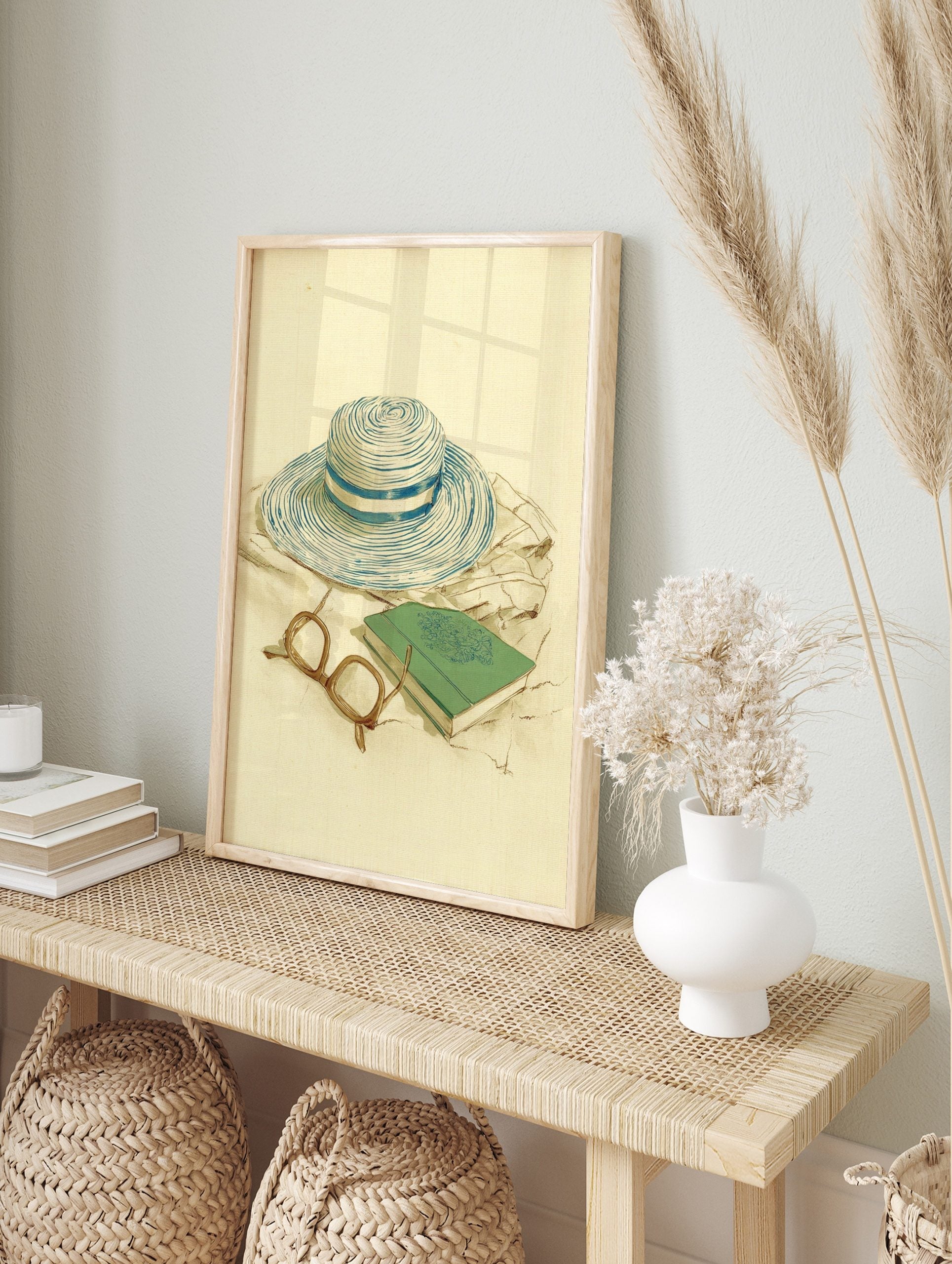 Illustrative print of a blue and white striped straw hat, green book, and eyeglasses on a, in an alternate framed mockup