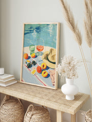 Illustrative summer still life with peaches, wine, water glass, sunglasses, and hat by a blue, in an alternate framed mockup