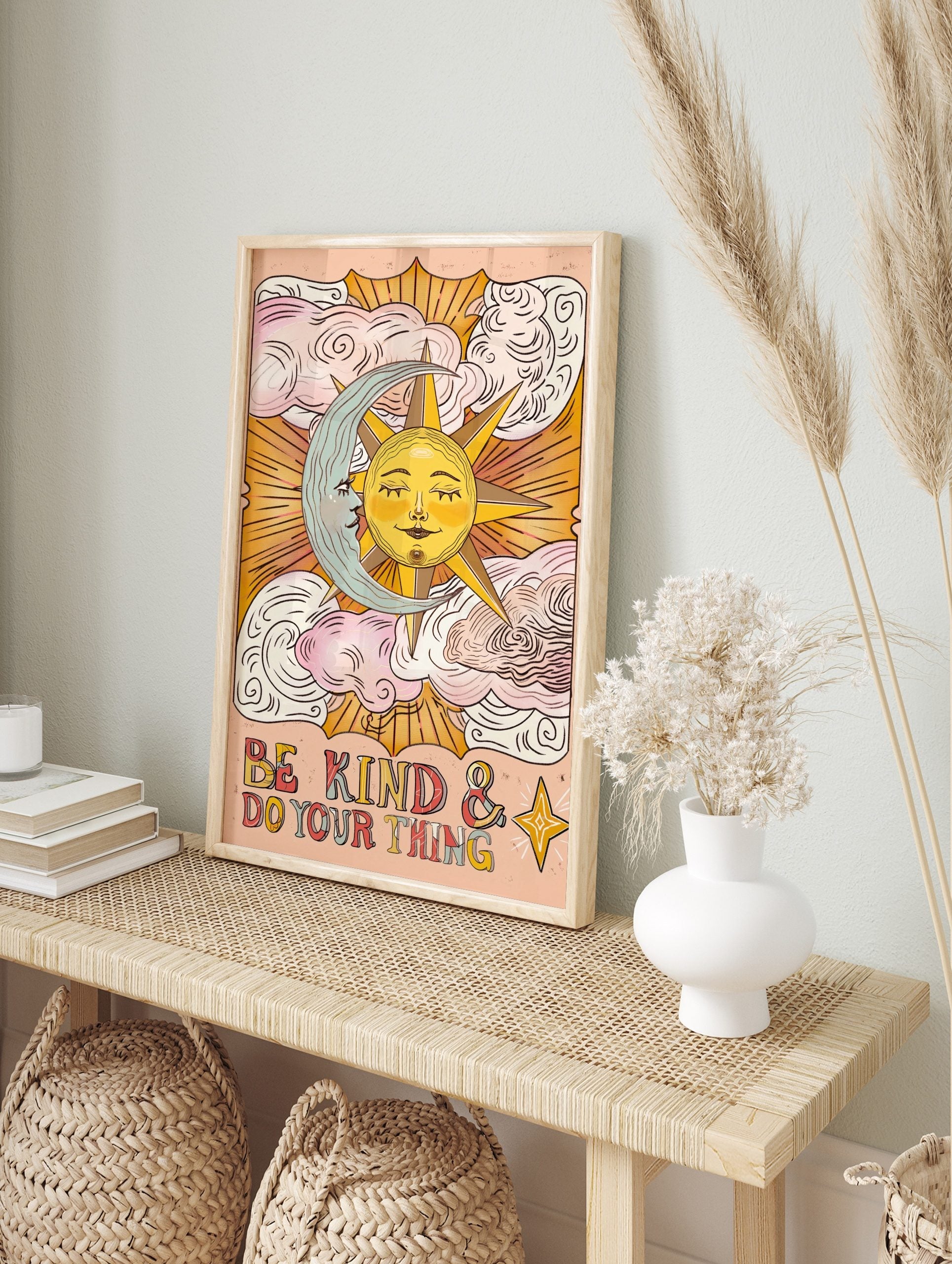 Celestial sun and moon wall art with 'Be Kind & Do Your Thing' text and clouds on a peach background, displayed as the same artwork in an alternate framed wall art mockup