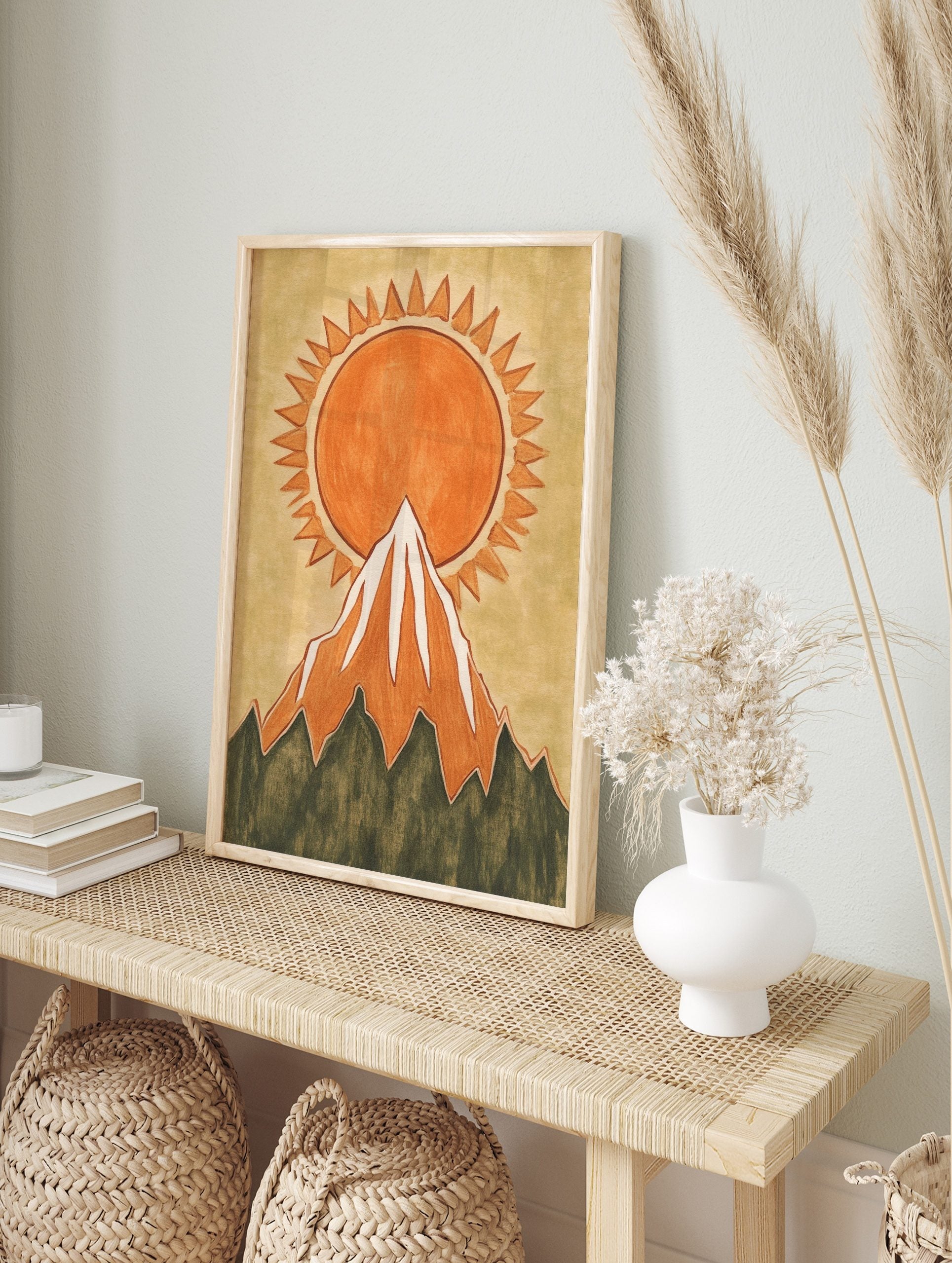 Illustrative orange sun with jagged rays rising behind a snow-capped mountain wall art print, in an alternate framed mockup