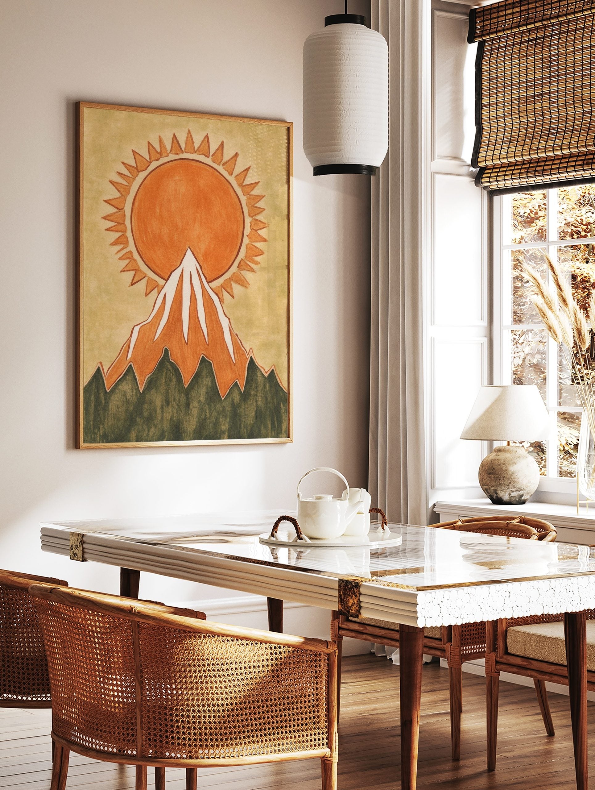 Illustrative orange sun with jagged rays rising behind a snow-capped mountain wall art print, in a styled room mockup