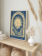 Illustrative sun face with closed eyes in an ornate arch with botanical leaves, blue and, in an alternate framed mockup