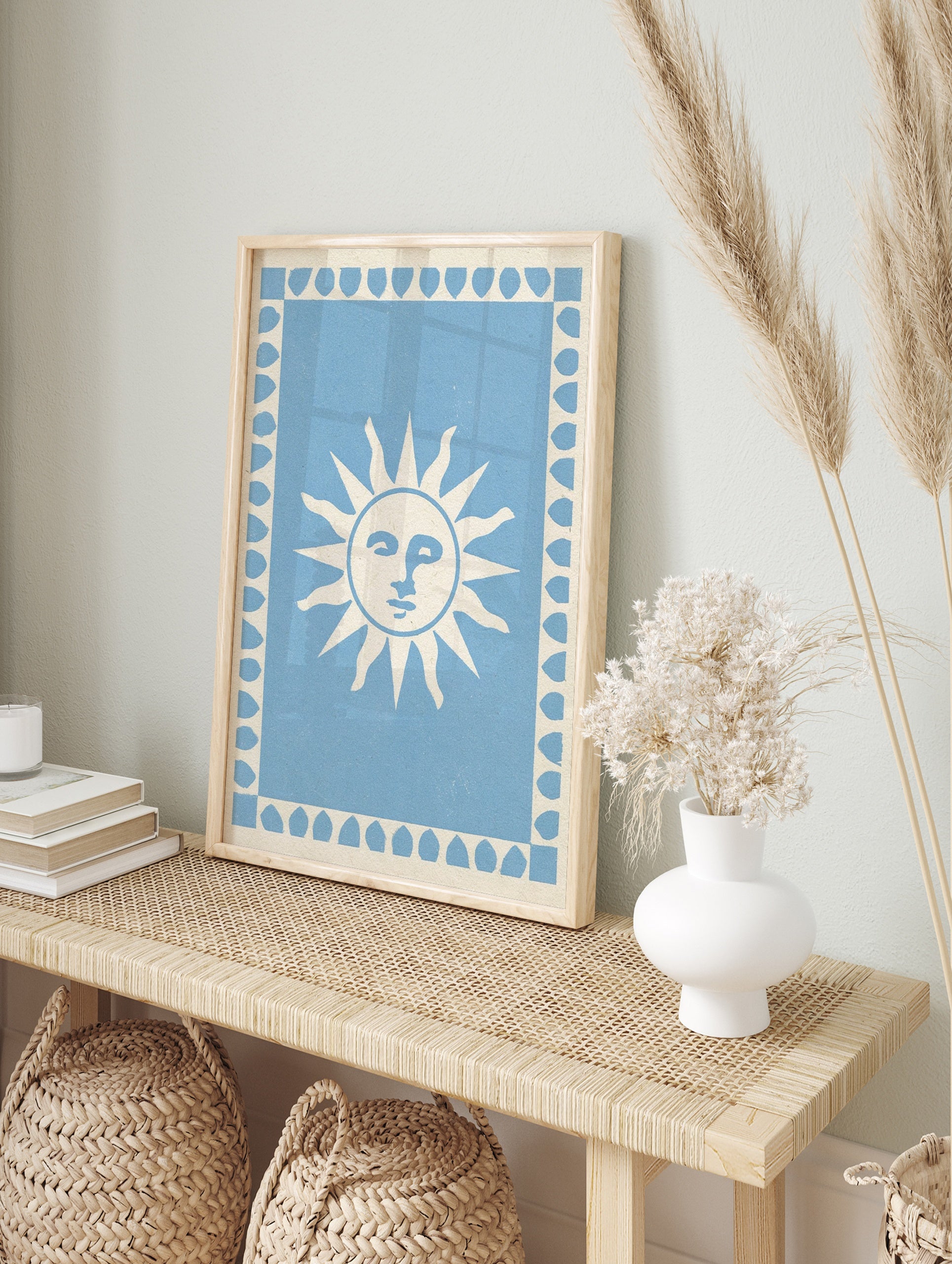 Stylized sun face illustration with a leaf border on a light blue background, art print, in an alternate framed mockup