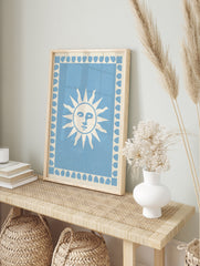 Stylized sun face illustration with a leaf border on a light blue background, art print, in an alternate framed mockup