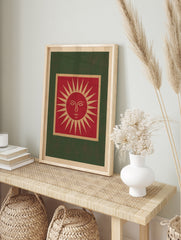 Illustrative red sun face wall art print with tan and green borders on a cream background, in an alternate framed mockup