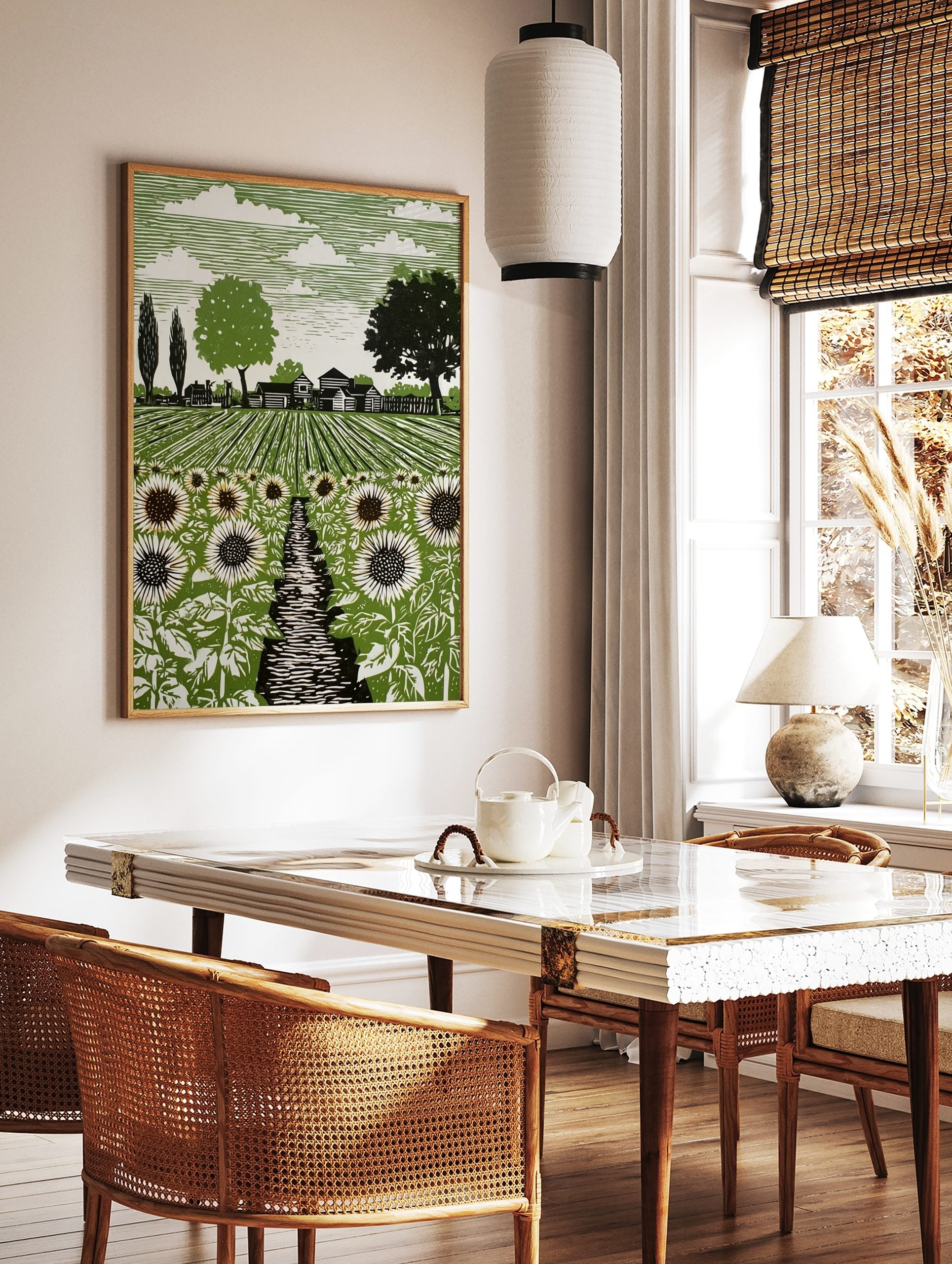 Linocut style art print of a sunflower field with a path, farmhouses, and trees under a striped sky, in a styled room mockup