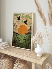 Linocut-style art print of two birds flying over an orange sun, green fields, and tall, in an alternate framed mockup