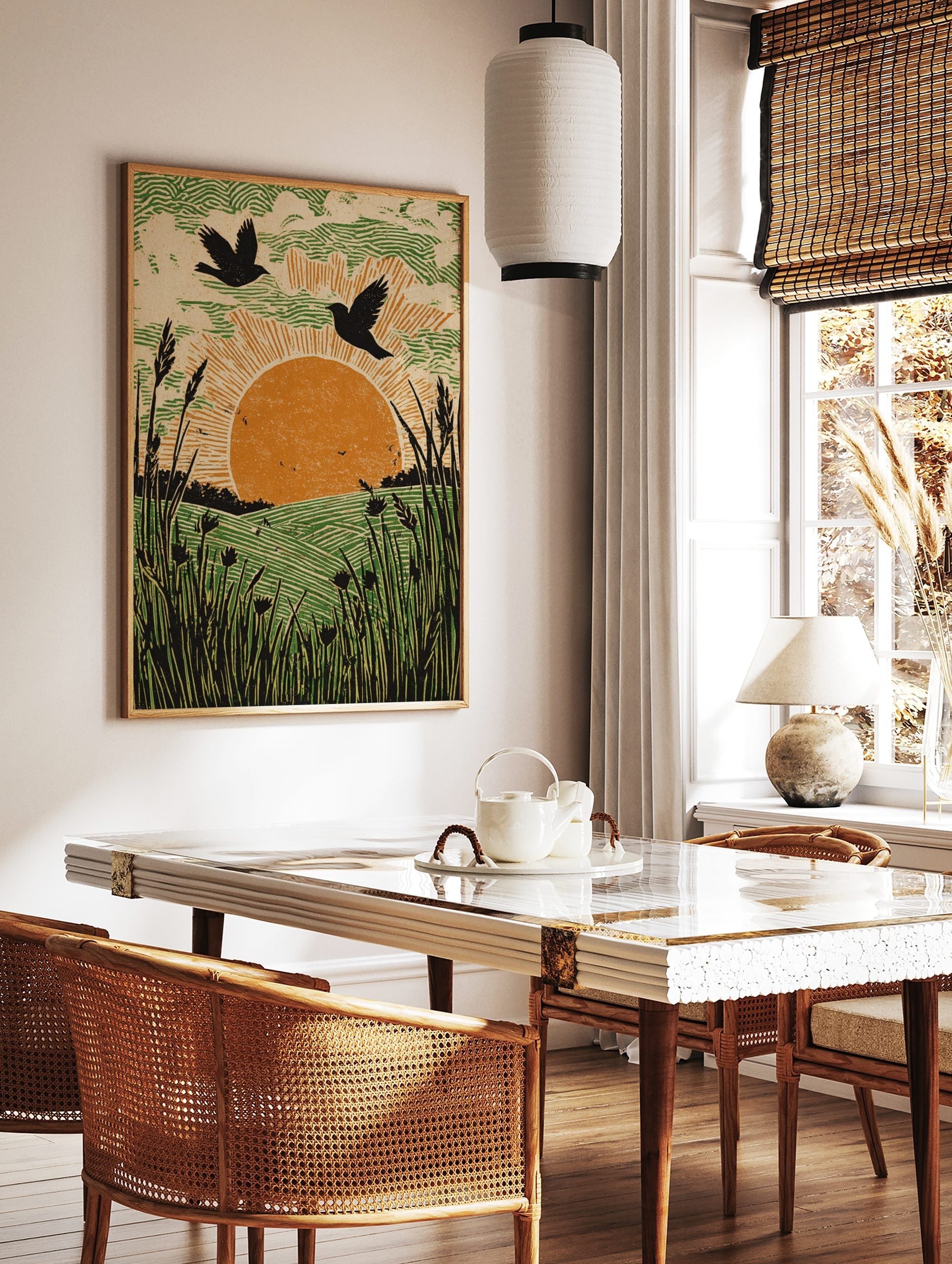 Linocut-style art print of two birds flying over an orange sun, green fields, and tall foreground, in a styled room mockup