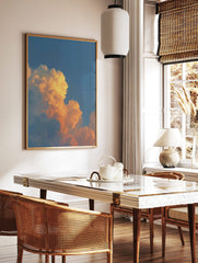 Dramatic orange and golden cumulus clouds against a clear blue sky during sunset, in a styled room mockup