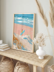 Impressionistic painting of surfer with blue board walking on pink beach towards ocean waves, in an alternate framed mockup