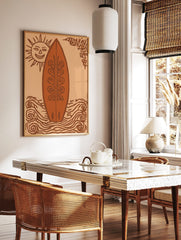 Illustrative art print of a decorative surfboard, smiling sun, and swirling waves in orange and, in a styled room mockup