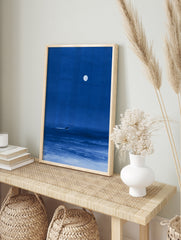 Minimalist blue night sea art print featuring a lone surfer gliding under a large full moon, in an alternate framed mockup