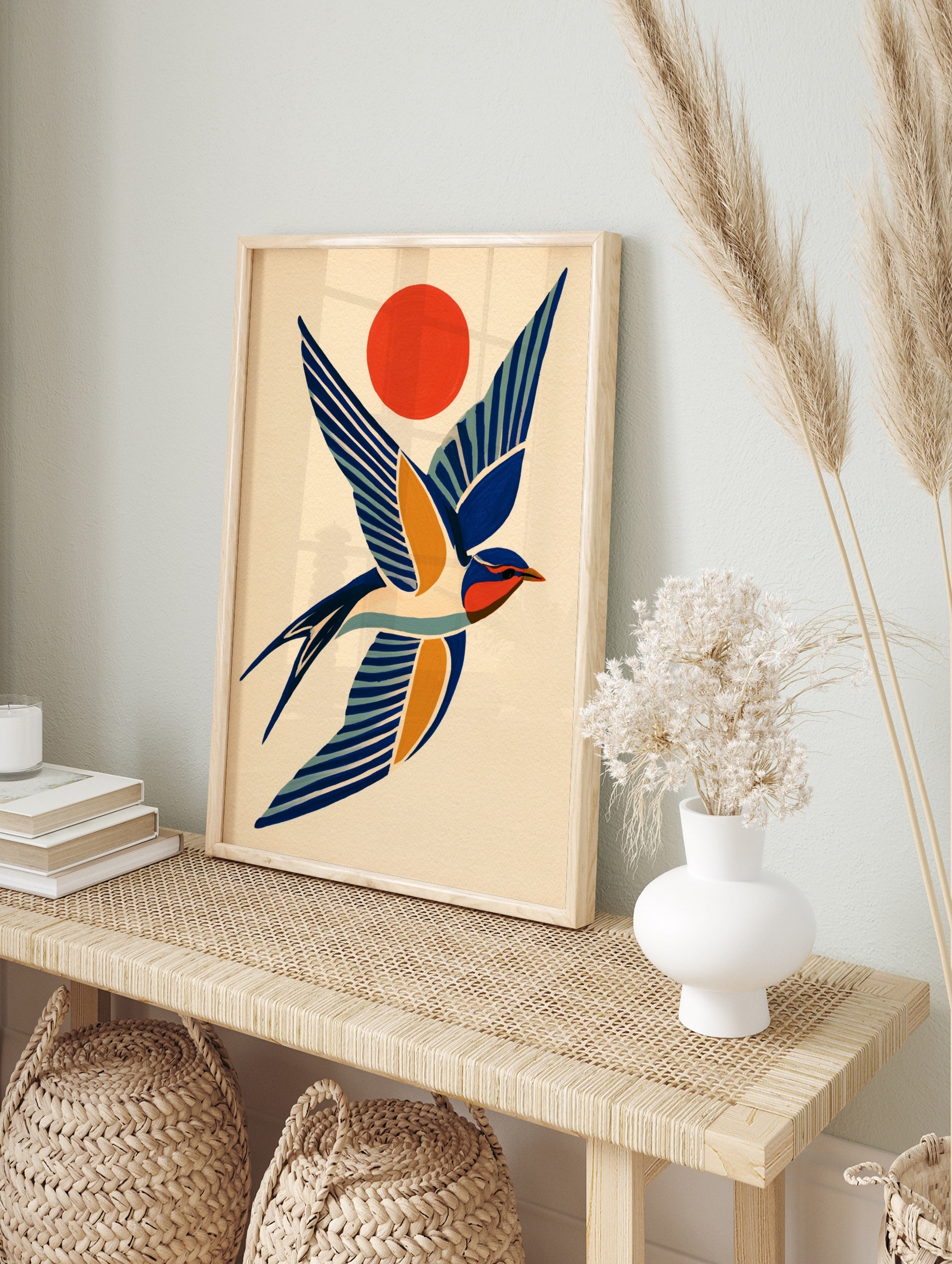 Stylised swallow bird illustration in blue and orange with a sun motif on a cream background, in an alternate framed mockup