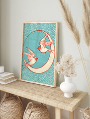 Vintage-style illustrative print of two swallows flying around a crescent moon against a, in an alternate framed mockup