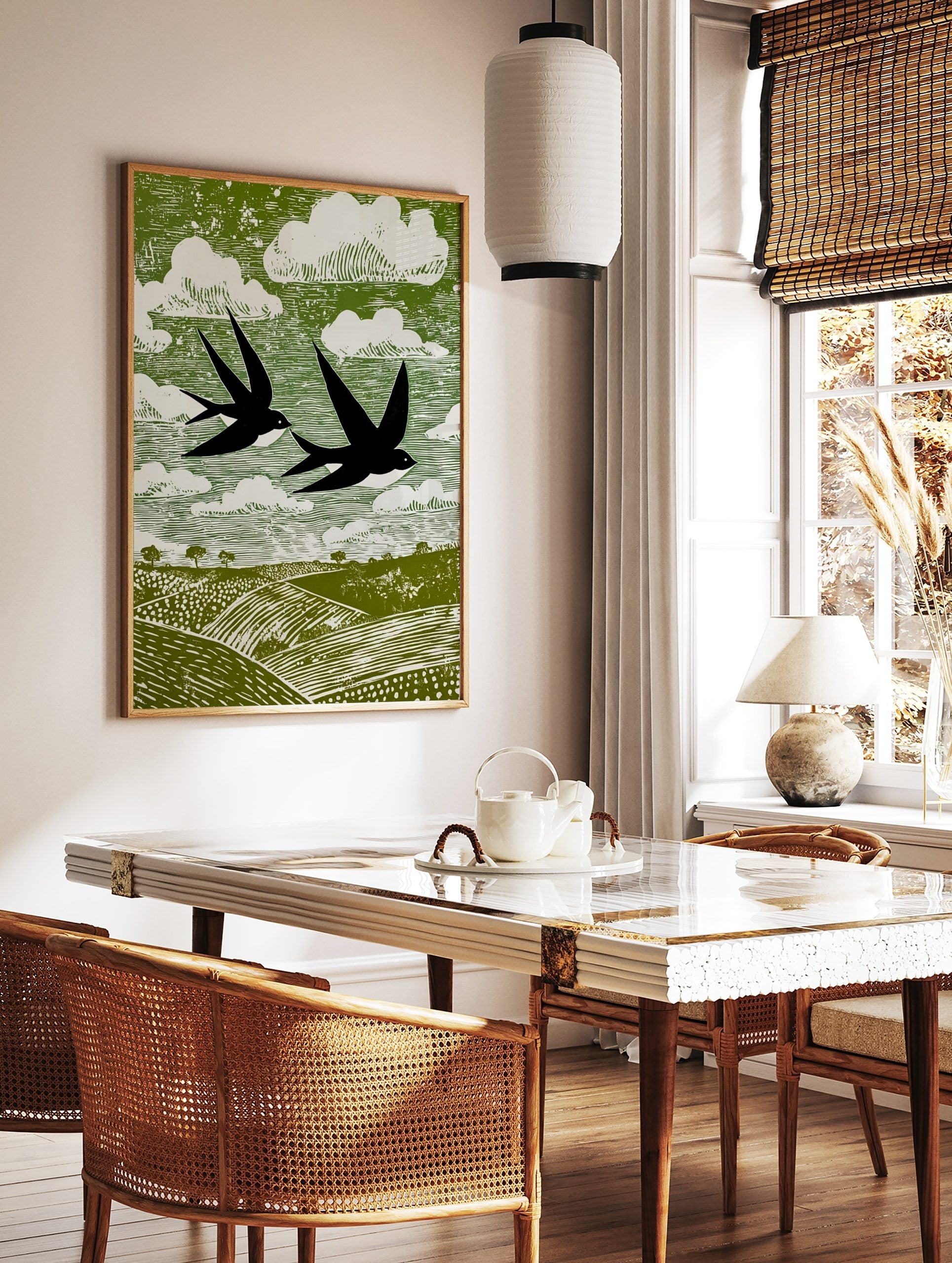 Stylised linocut print of two black swallows flying over green fields and white clouds in a green, in a styled room mockup