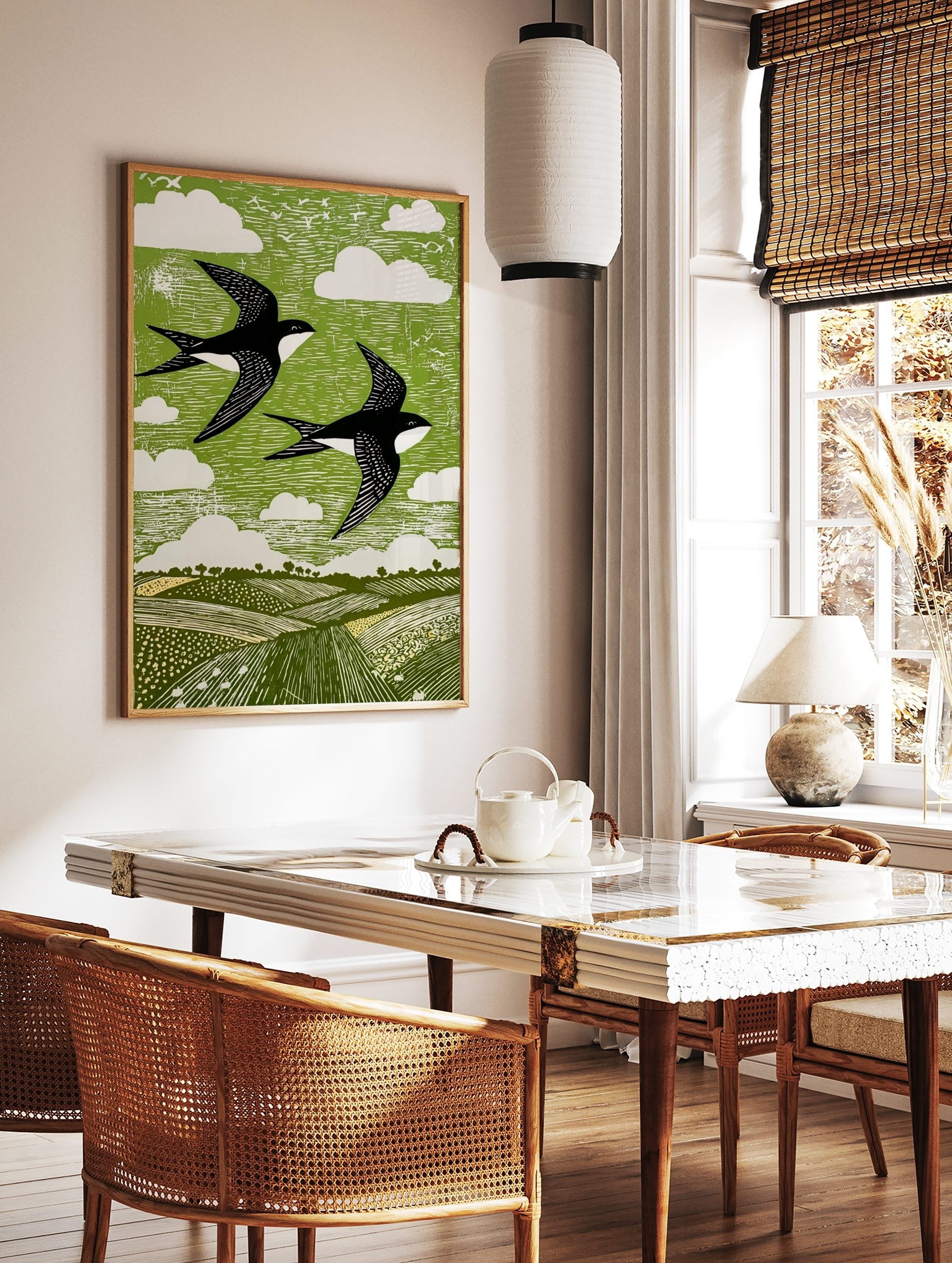 Linocut style print of two black and white swallows flying over green fields and sky with white, in a styled room mockup