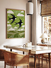 Linocut style print of two black and white swallows flying over green fields and sky with white, in a styled room mockup