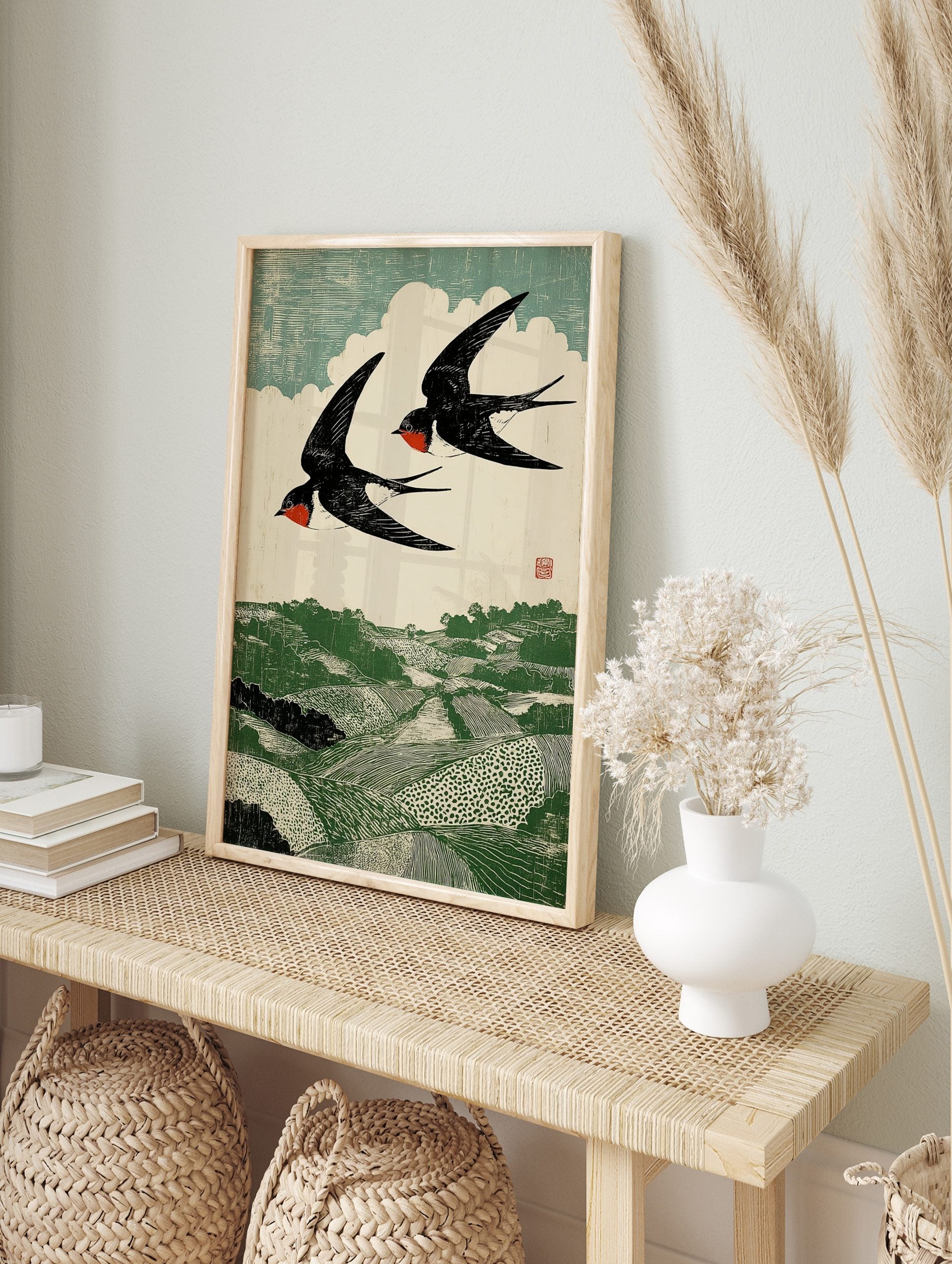 Woodcut print of two black and red swallows flying over a green rolling landscape with fields, in an alternate framed mockup