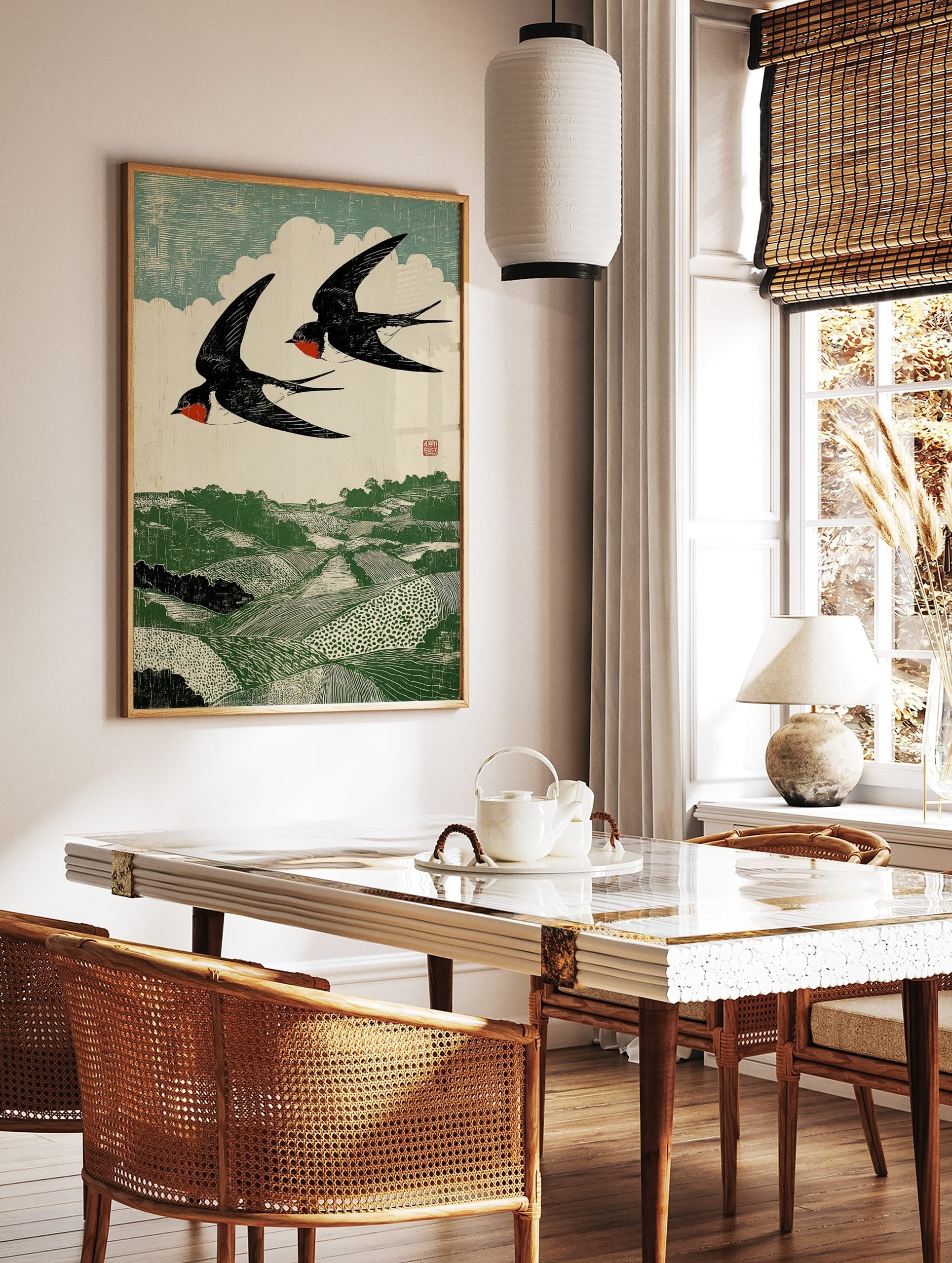 Woodcut print of two black and red swallows flying over a green rolling landscape with fields and, in a styled room mockup