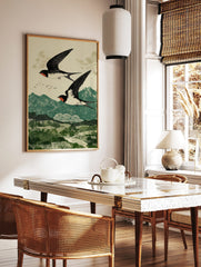 Two black and white swallows with red markings flying over green mountains in a woodblock print, in a styled room mockup