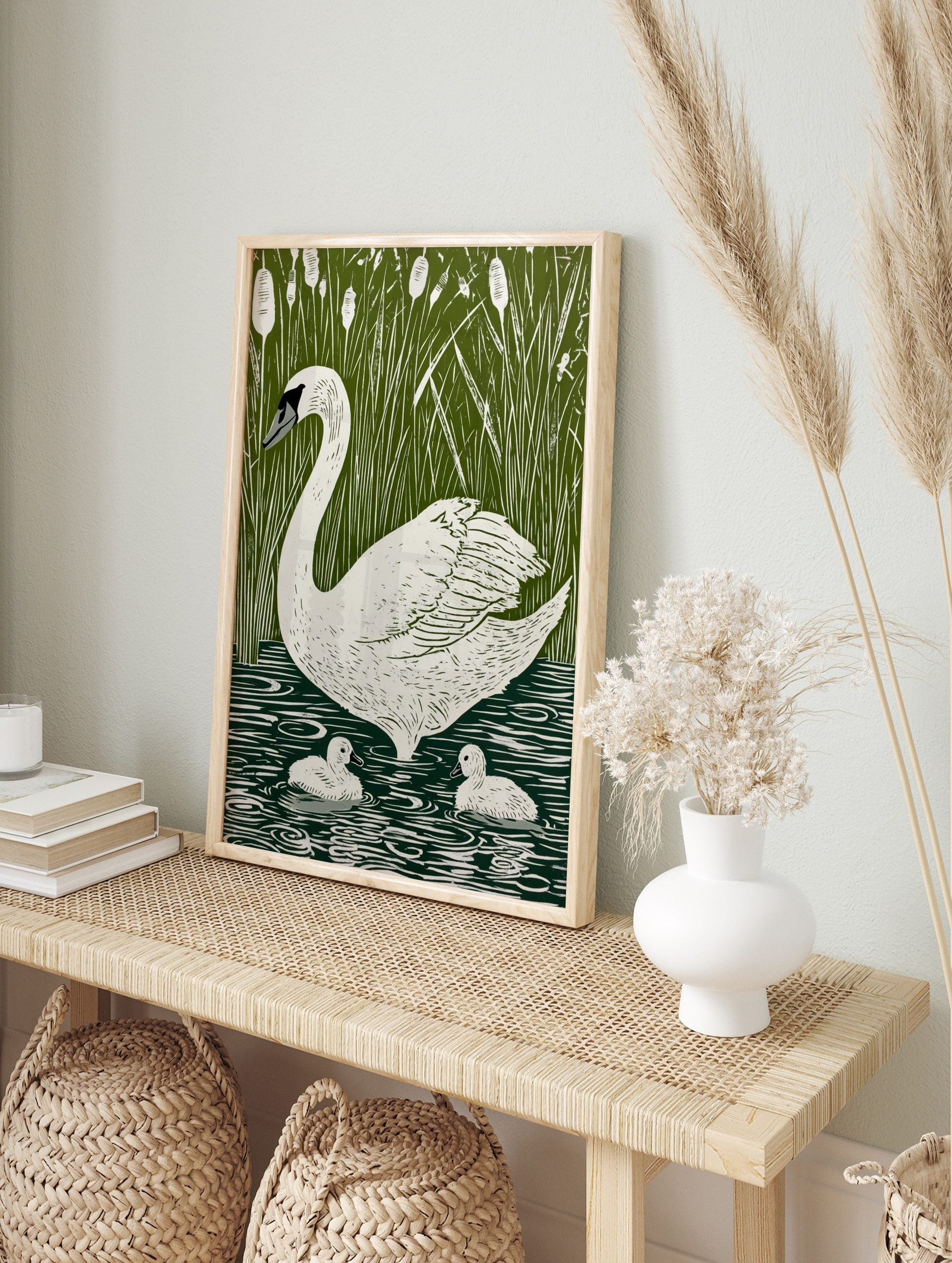 White swan and two cygnets swimming in green water with tall reeds and cattails in, in an alternate framed mockup