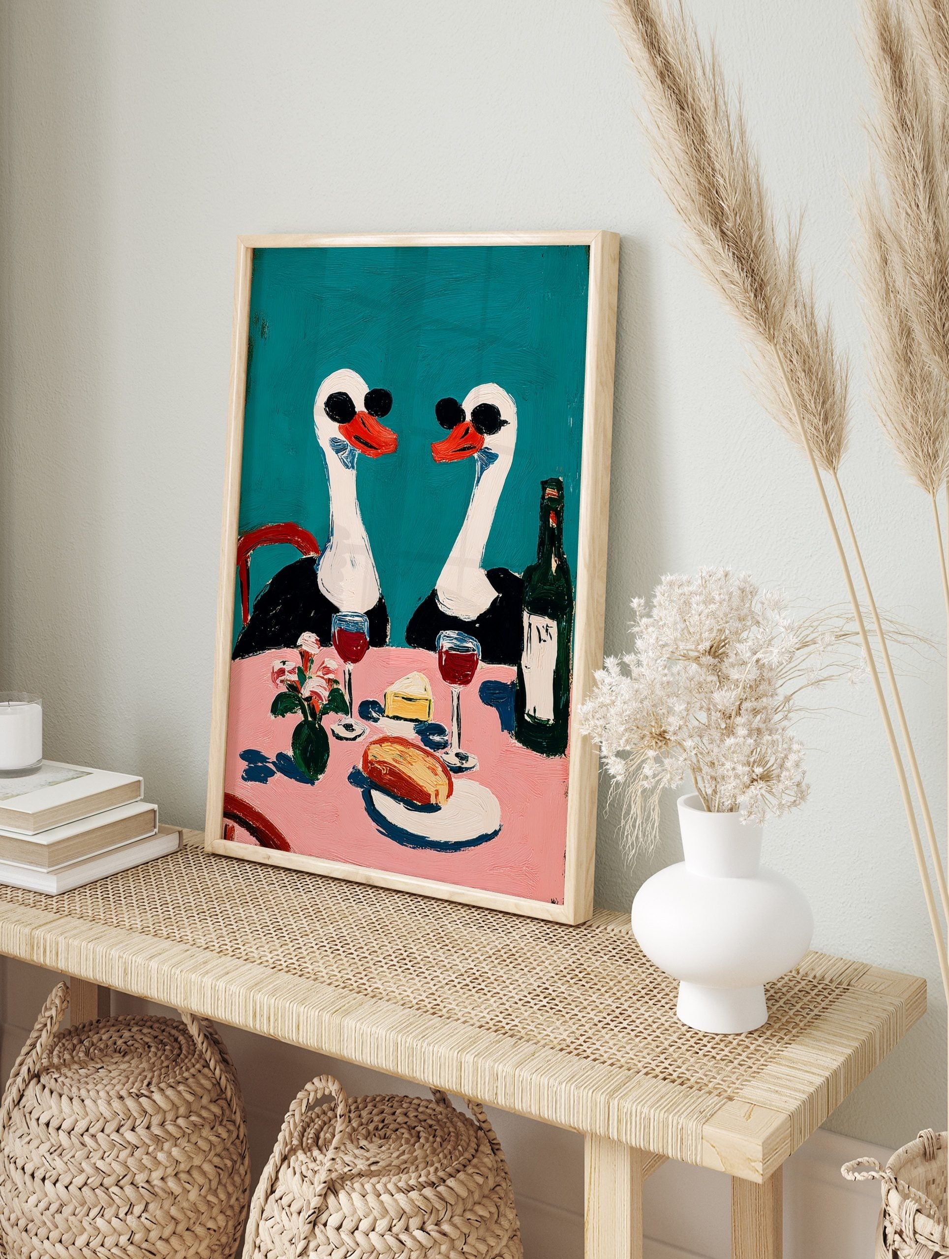 Painterly wall art of two swans in sunglasses at a pink dining table with wine, cheese, and, in an alternate framed mockup