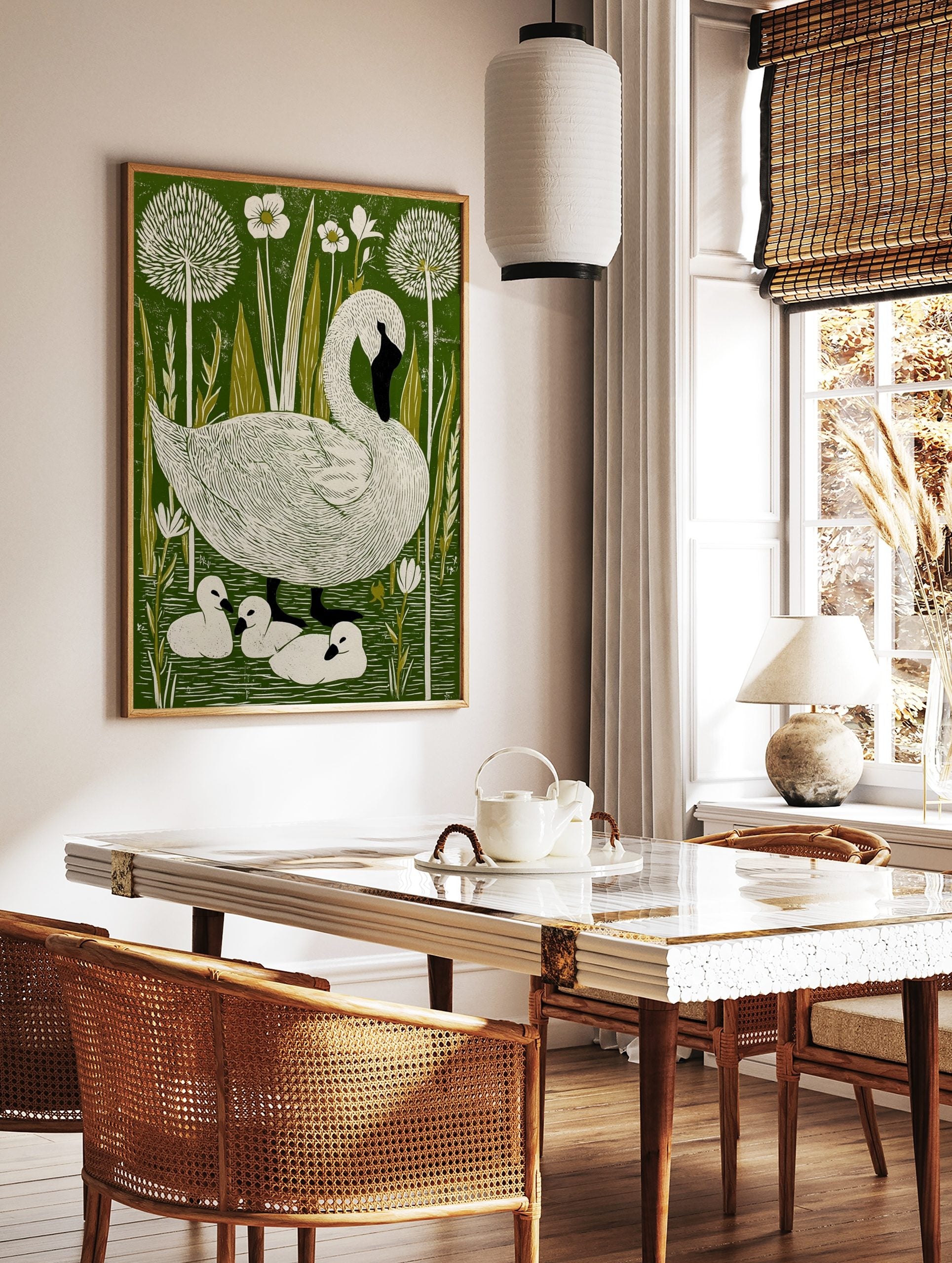 Illustrative linocut-style print of a white swan and three cygnets in a green pond with white, in a styled room mockup