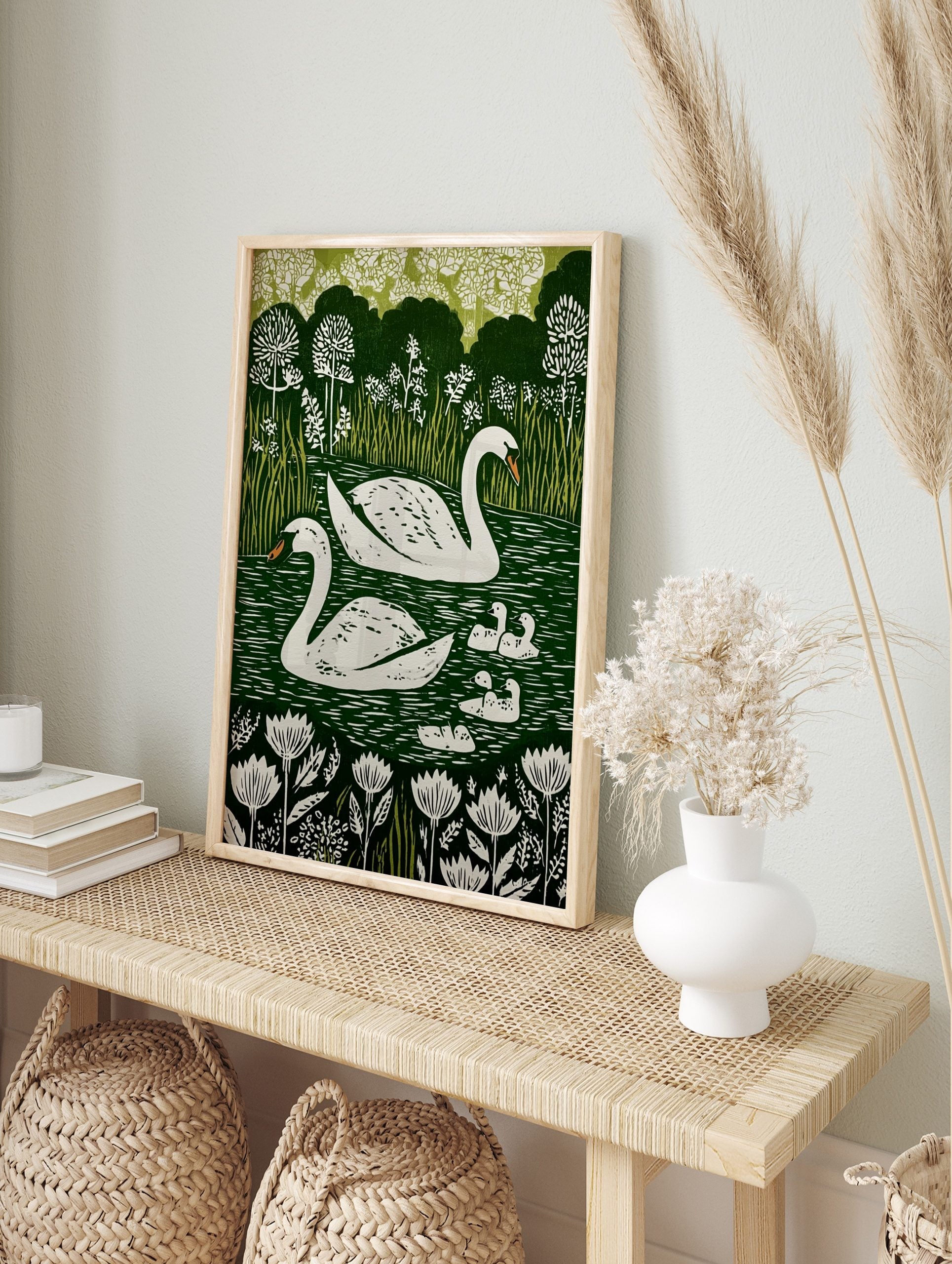 Illustrative print of two white swans and five cygnets on a dark green lake with white, in an alternate framed mockup