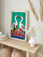 Illustrative print of two white swans with red beaks over a pink floral dinner table with, in an alternate framed mockup