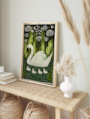 White swan with four cygnets swimming on green water, surrounded by green reeds and white, in an alternate framed mockup