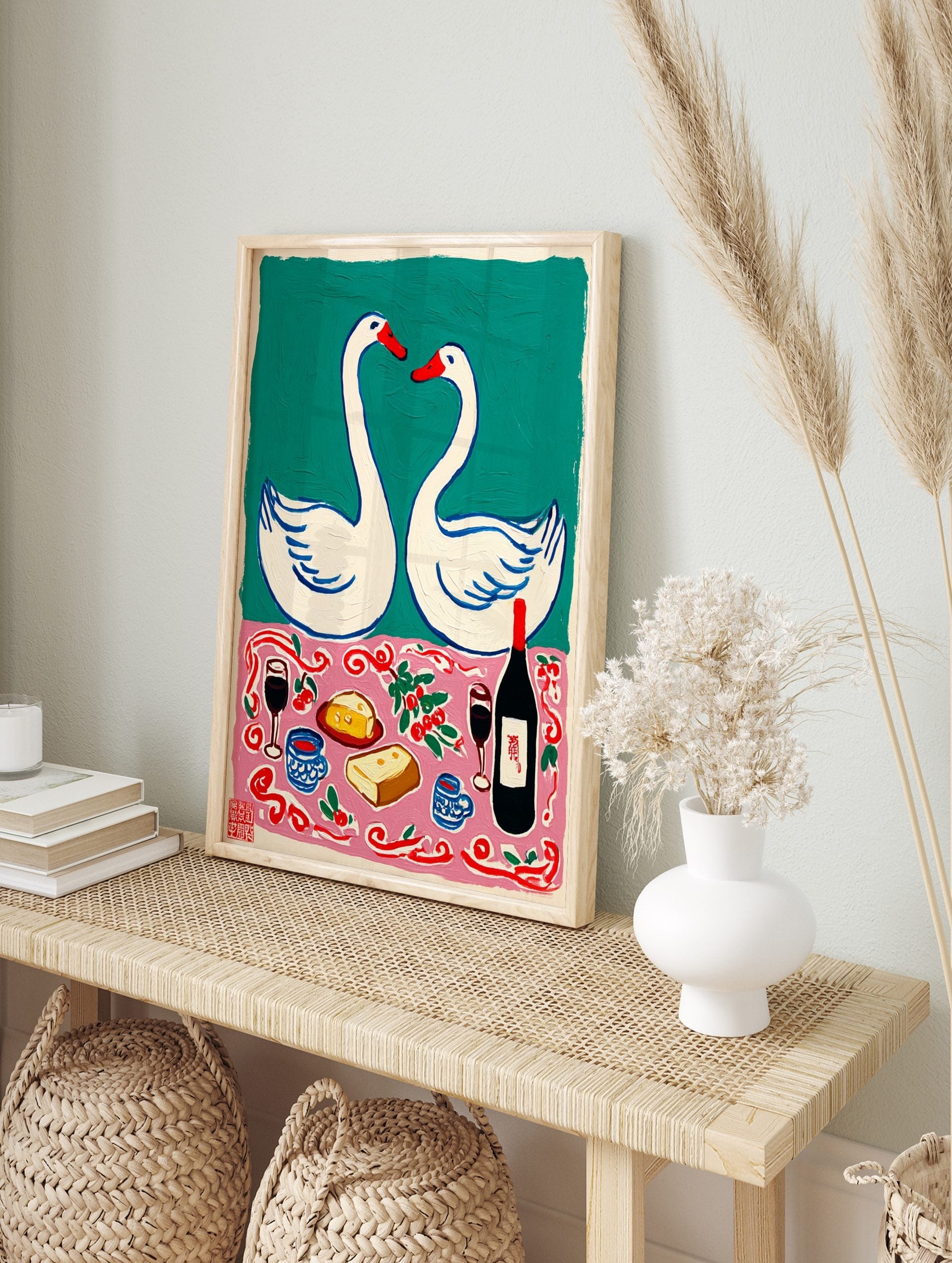 Illustrative print of two white swans forming a heart above a pink tablecloth with wine, in an alternate framed mockup
