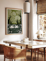 Linocut print of two white swans on water, surrounded by green trees and botanical leaves, forming, in a styled room mockup