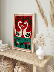 Illustrative wall art of two white swans with wine glasses, forming a heart, against a red, in an alternate framed mockup