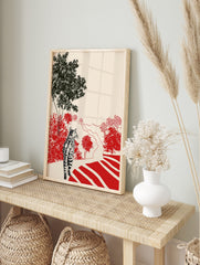 Tabby cat on path looking at red bushes and black trees in illustrative landscape print, in an alternate framed mockup
