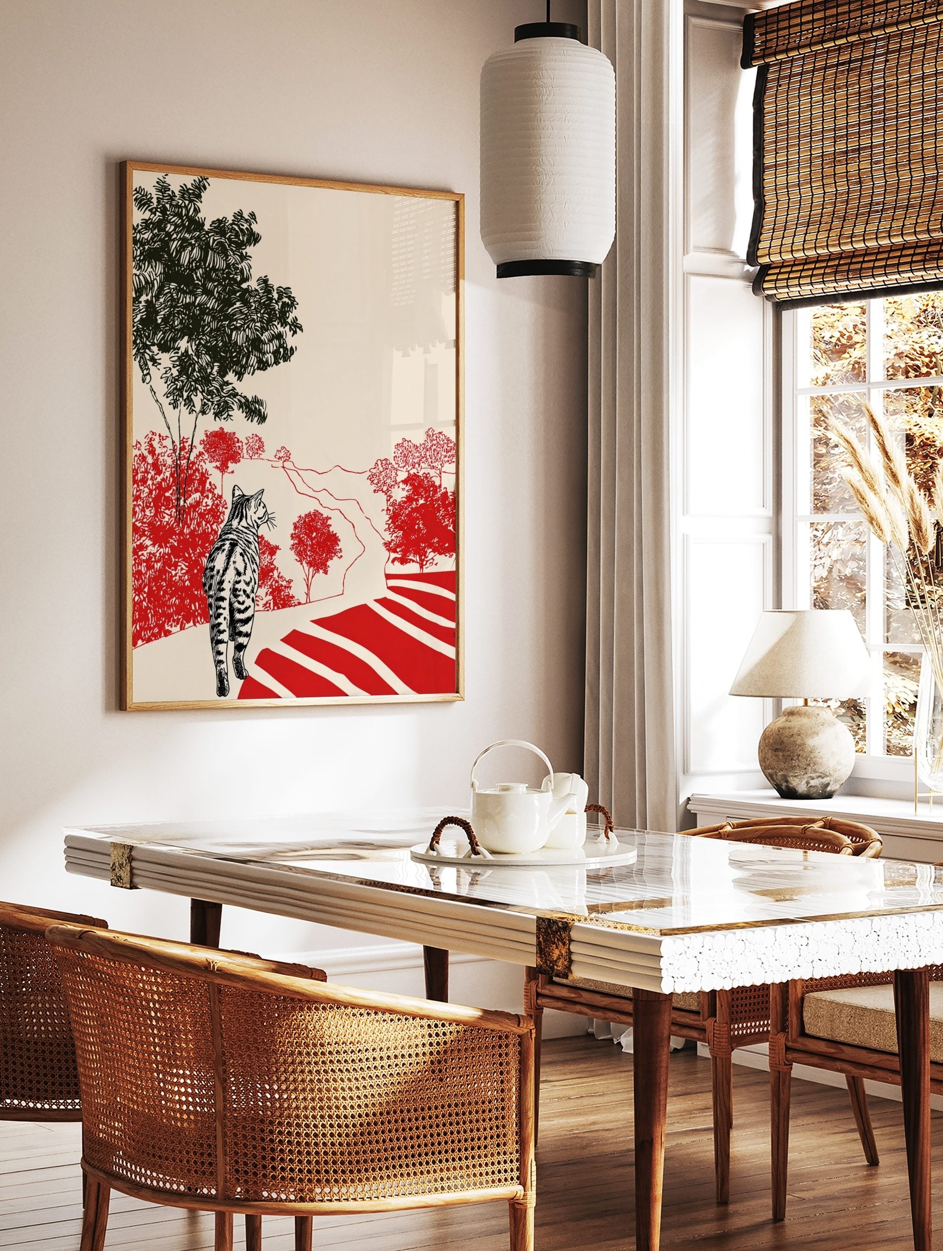 Tabby cat on path looking at red bushes and black trees in illustrative landscape print, in a styled room mockup