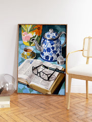 Still life painting with blue floral teapot, teacup, open book with glasses, and a vibrant floral vase. - Image 2