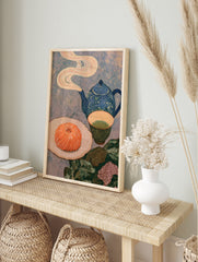 Still life art print with a blue teapot, green tea, and a swirled orange pastry on a textured, in an alternate framed mockup