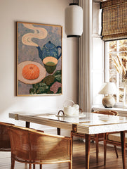 Still life art print with a blue teapot, green tea, and a swirled orange pastry on a textured, in a styled room mockup