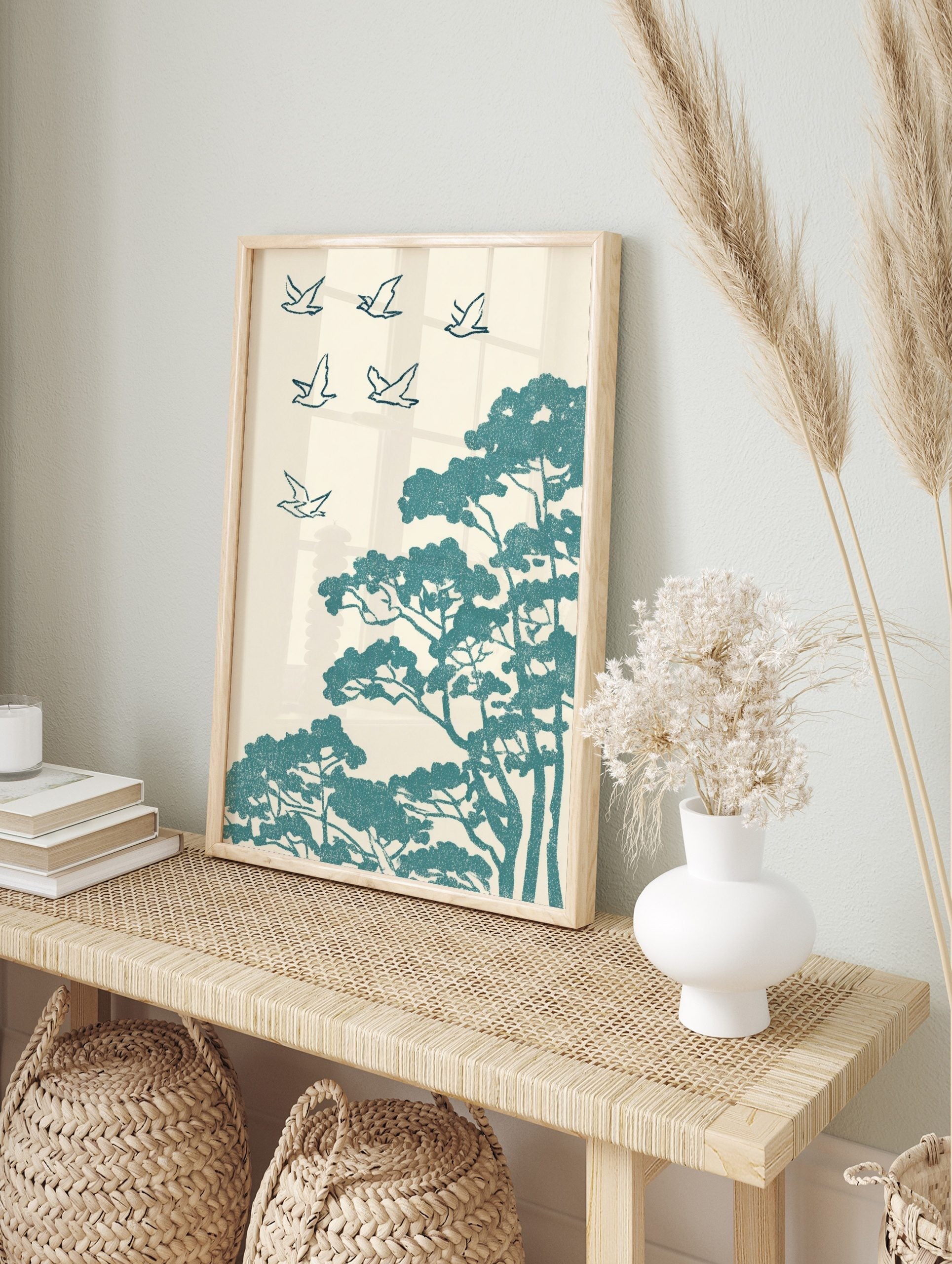 Teal stylised birds flying above pine trees in an illustrative, textured Japanese art print, in an alternate framed mockup