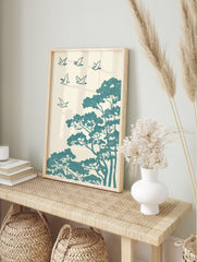 Teal stylised birds flying above pine trees in an illustrative, textured Japanese art print, in an alternate framed mockup