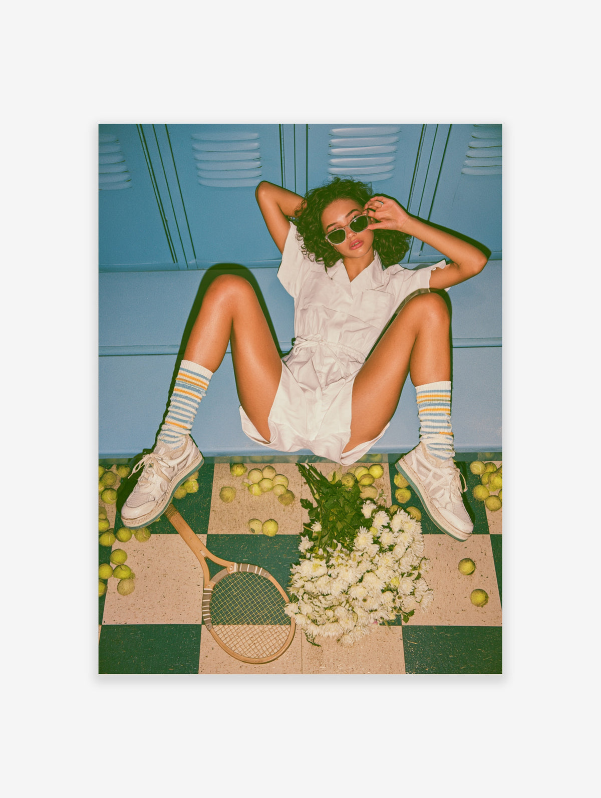 Woman in white tennis outfit sitting on blue locker room floor with racket, apples, and flowers
