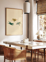 Three illustrative frogs with floral, solid, and striped patterns in green and gold on a beige, in a styled room mockup