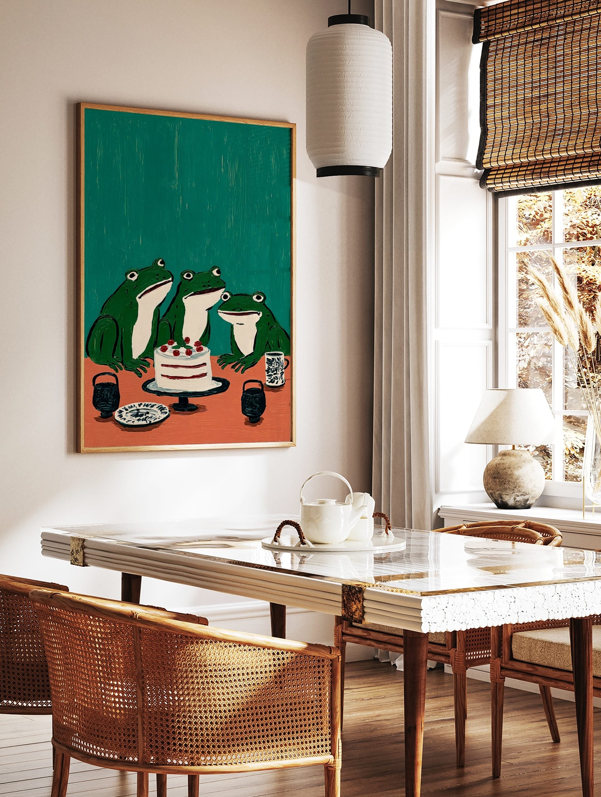 Illustrative wall art featuring three green frogs looking at a white cake with red berries on an, in a styled room mockup
