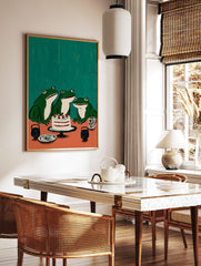 Illustrative wall art featuring three green frogs looking at a white cake with red berries on an, in a styled room mockup